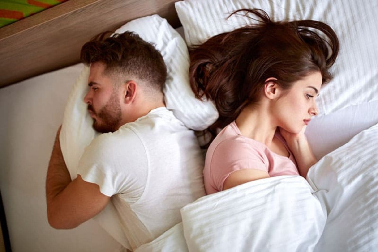 the man and woman lie on the bed with their backs to each other