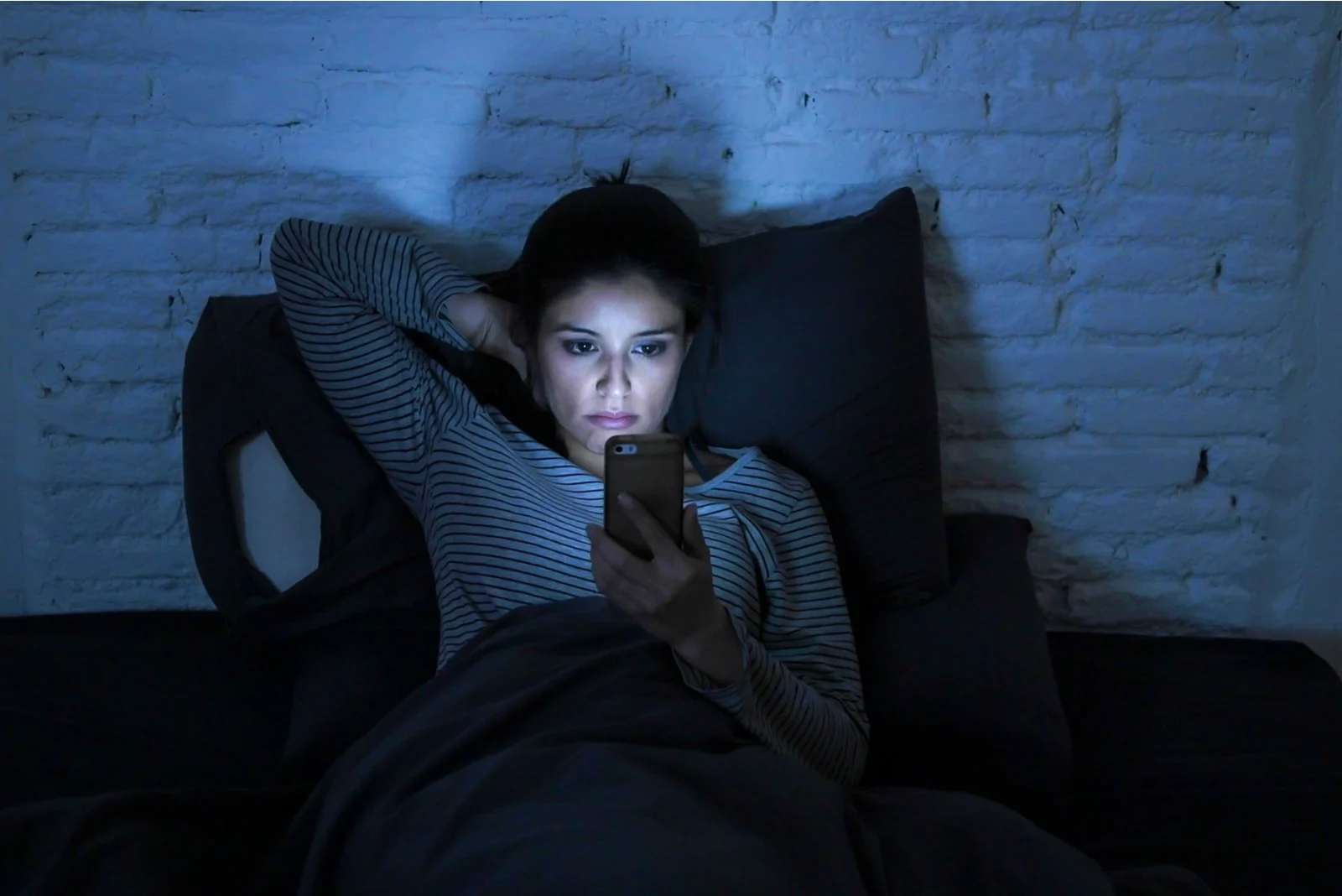 the night before bed a sad woman lies in bed and uses a smartphone