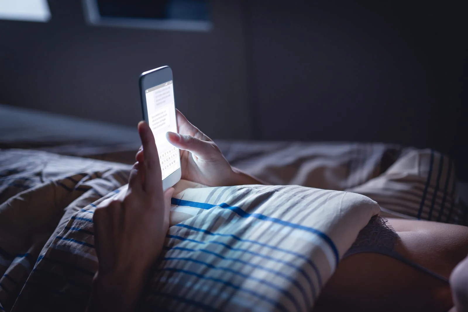 the woman lies in bed at night and reads a message on her smartphone