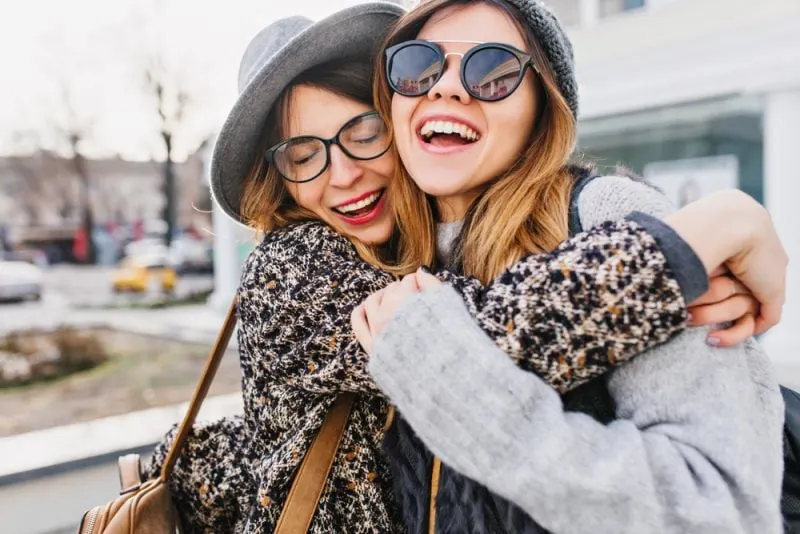 two stylish girls hugging on street