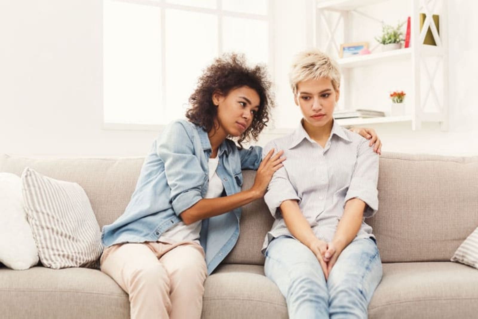 two women sit on the couch and comfort her