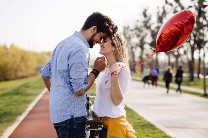 woman holding balloon with shape of heart while looking at her boyfriend