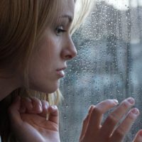 sad young blonde woman by the window looking outside