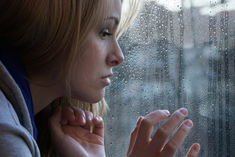 joven rubia triste junto a la ventana mirando al exterior