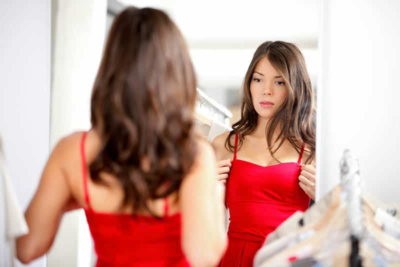 Young brunette woman looking at herself in the mirror trying on a dress