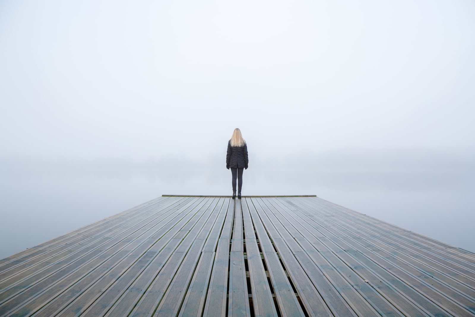 Giovane donna in piedi da sola sul bordo della passerella e con lo sguardo rivolto al lago