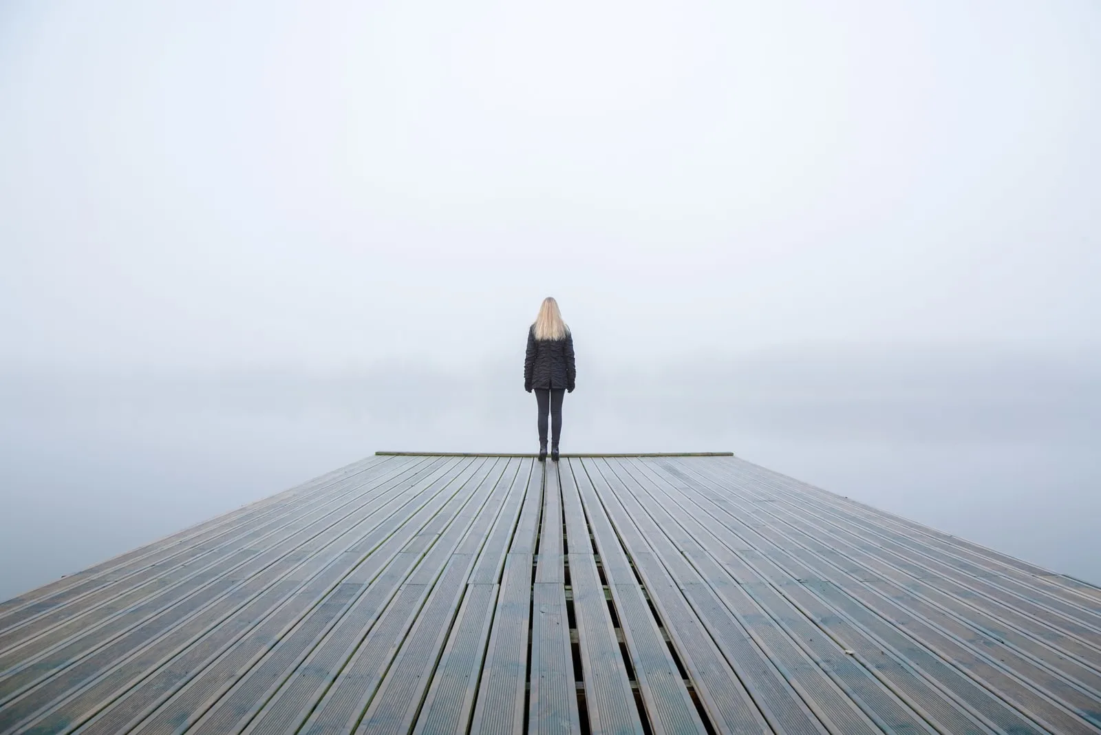 Young woman standing alone on edge of footbridge and staring at lake
