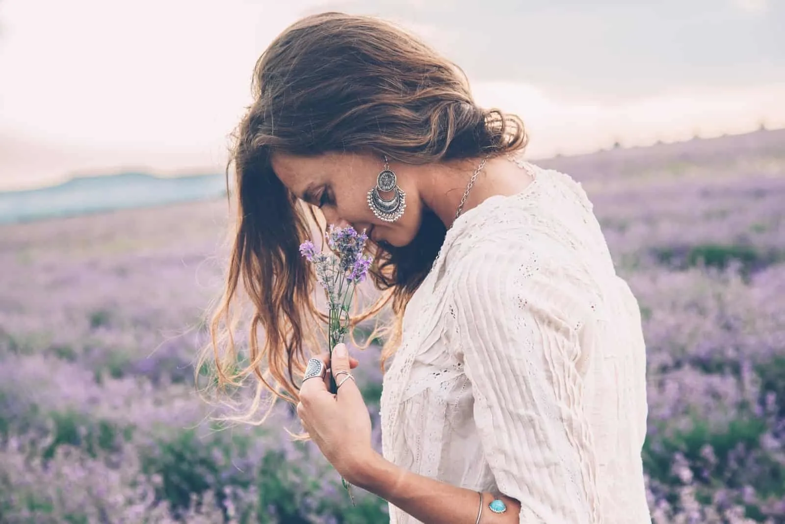 a beautiful woman walks through a lavender field and smells a lavender flower
