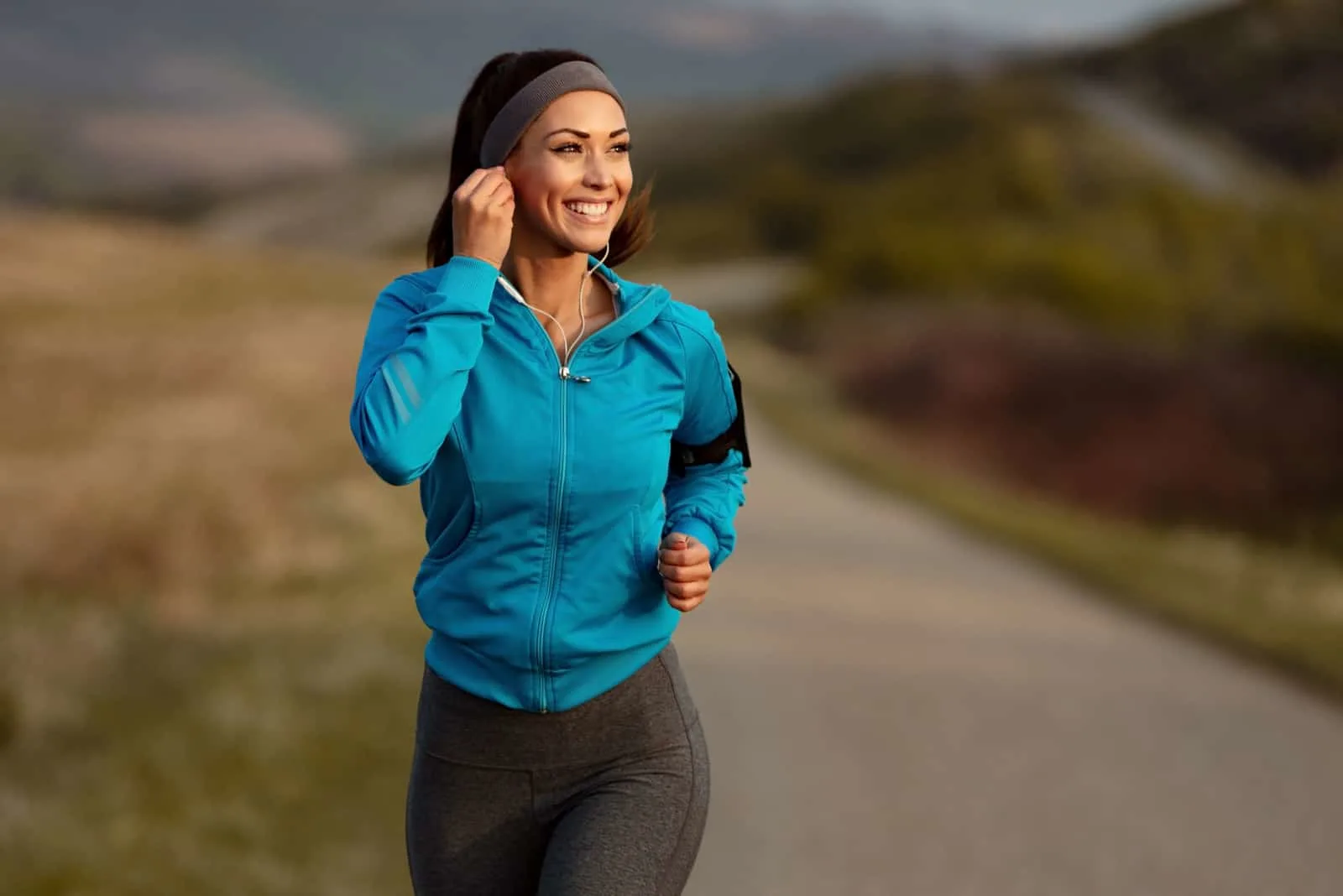 a smiling woman with headphones on her ears running