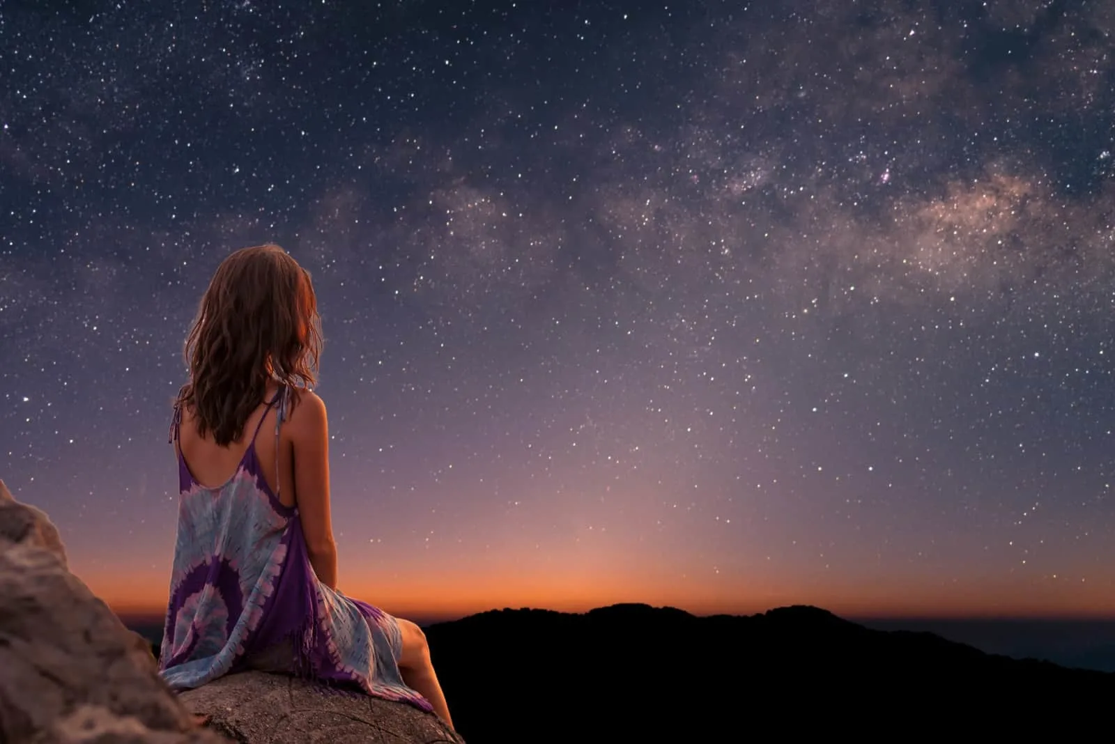 a woman sits on a rock and watches the stars in the sky