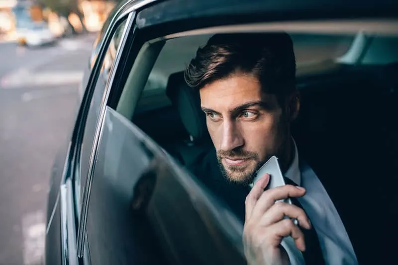 business man with a phone in his hand driving in the back of a car 