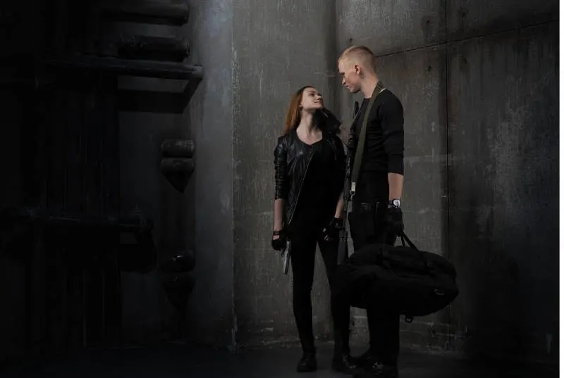 girl and guy in black clothes with guns and bag
