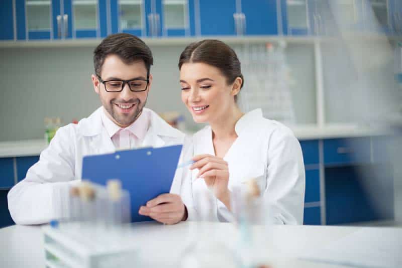 retrato de científicos sonrientes escribiendo en un bloc de notas en un laboratorio