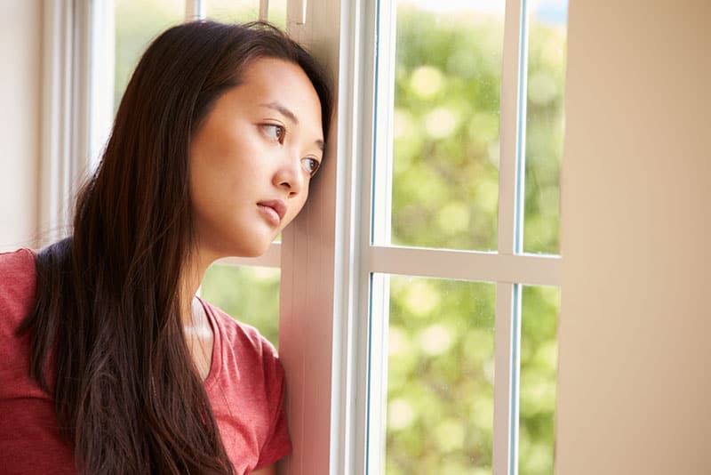 donna asiatica triste che guarda attraverso la finestra