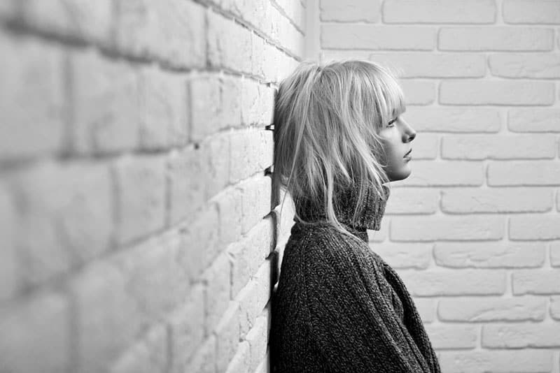 black and white picture of a sad young blonde woman leaning against the wall