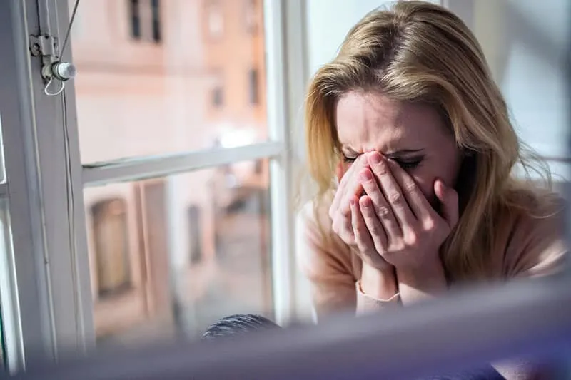 sad blonde woman crying by the window
