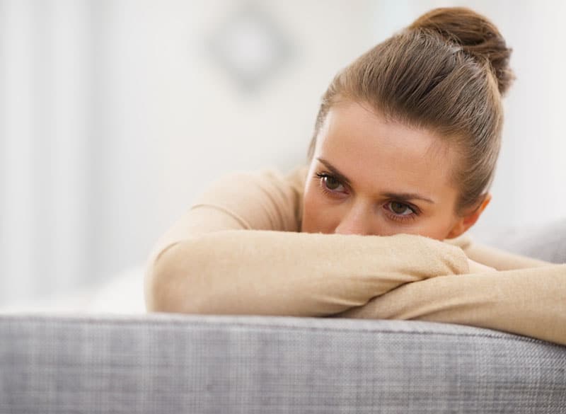 joven triste sentada en el sofá y tapándose la cara con el brazo