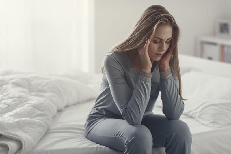 giovane donna bionda triste seduta sul letto