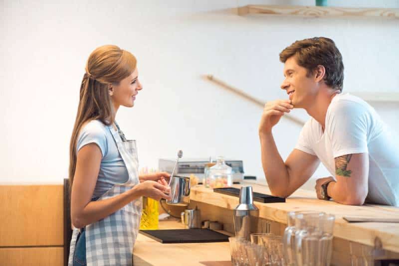 vista lateral de um jovem e uma mulher a namoriscarem num café