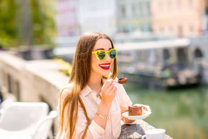 mujer sonriente comiendo tarta de chocolate cerca del río