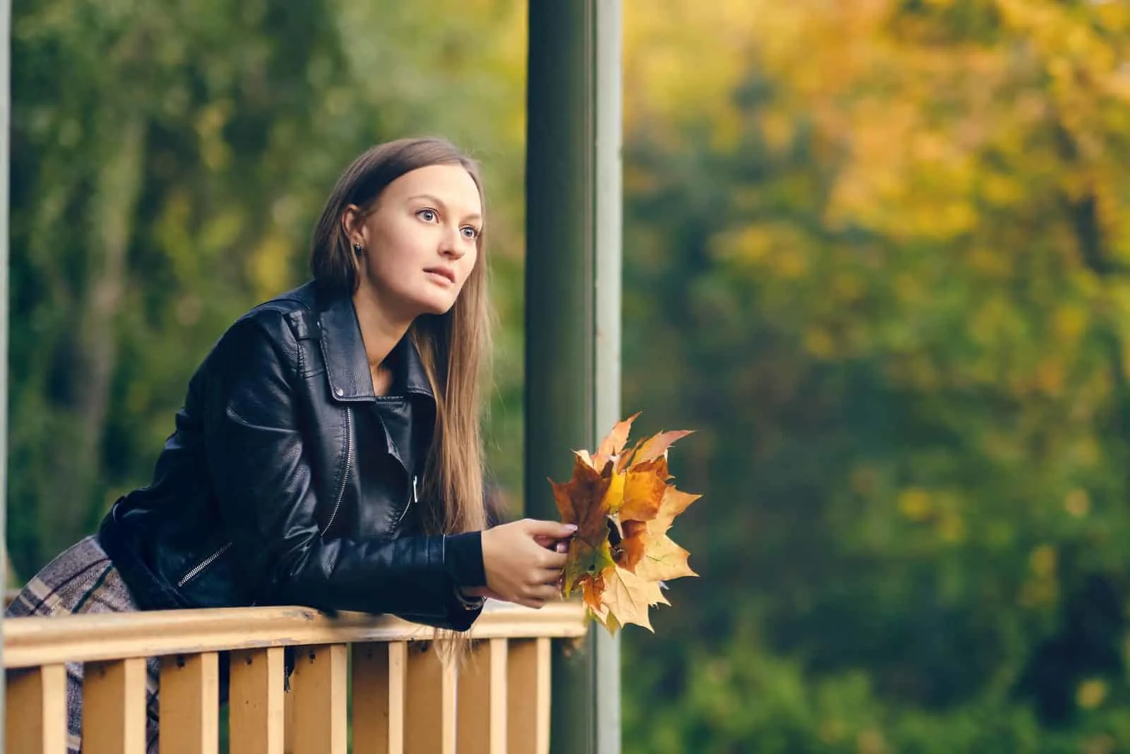 the woman stands on the terrace with leaves in her hands and thinks anxiously