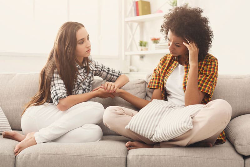 woman comforting her sad friend on a couch