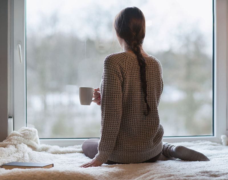 mulher com café a olhar pela janela