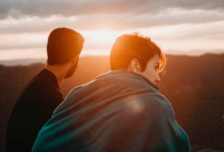 vista traseira de homem e mulher em frente ao pôr do sol