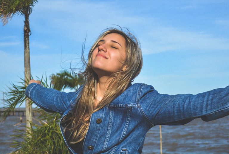 Female in denim jacket arms spread out chin up and eyes closed