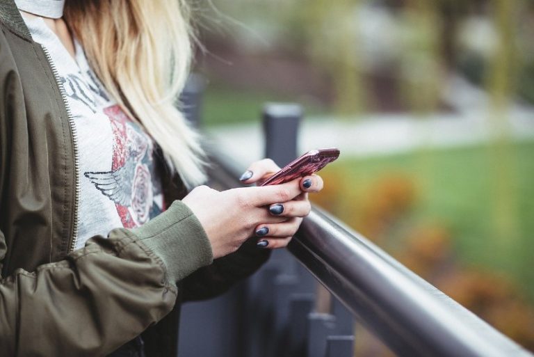 Blonde girl with khaki jacket holding smartphone