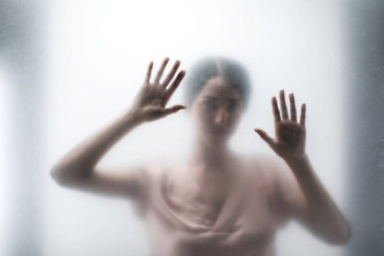 Silhouette of woman behind glass and touching it with hands