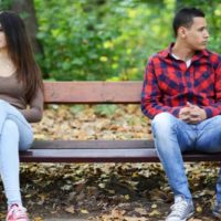 young upset couple sitting on a park bench