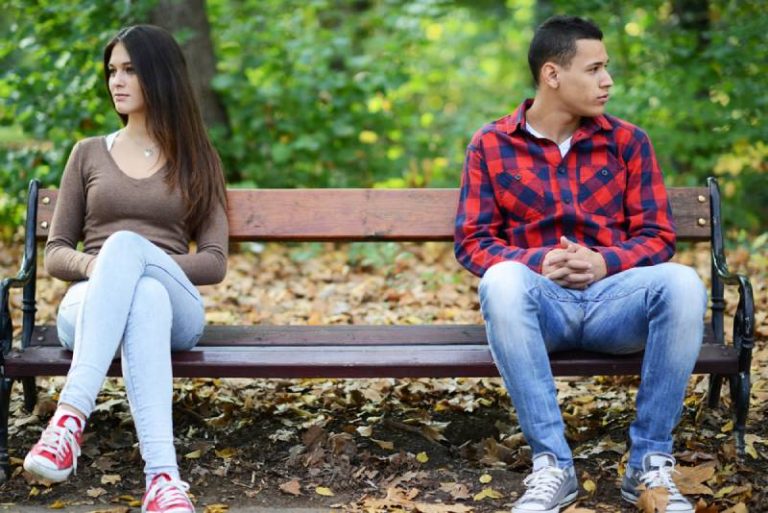jovem casal aborrecido sentado num banco de jardim