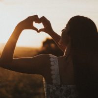 young girl making a heart with her hands on the sunset