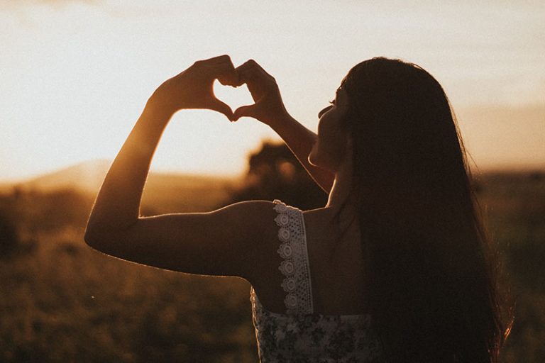 young girl making a heart with her hands on the sunset