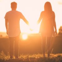 Couple holding hands facing the sunset