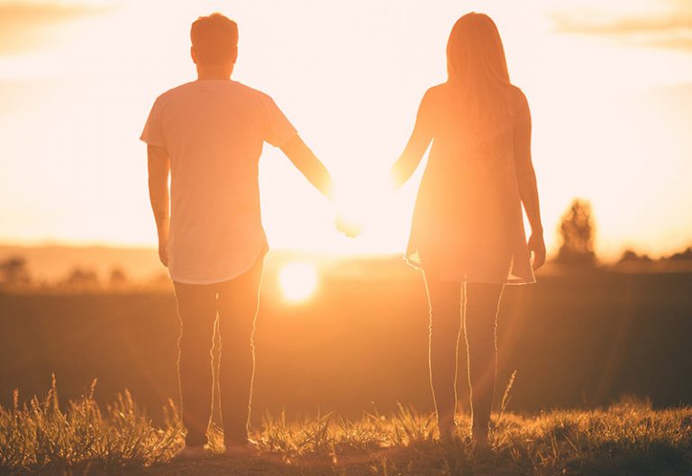Casal de mãos dadas a olhar para o pôr do sol