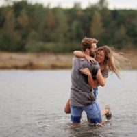 man hugging laughing woman while standing in water