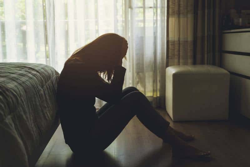 Giovane donna sola, depressa e stressata, seduta con la testa tra le mani in una camera da letto buia