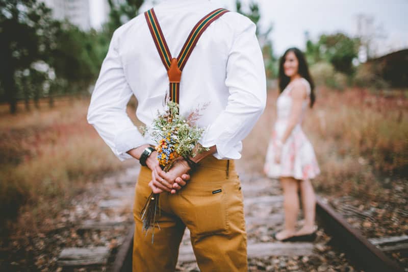 Man holding bouquet of wild flowers behind him