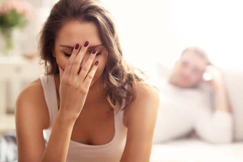 sad woman holding her hand while her man is behind on couch
