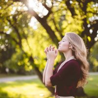 mujer rubia rezando en la naturaleza