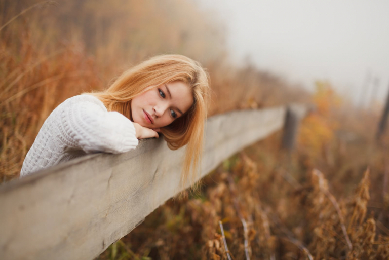 mujer rubia triste de pie junto a la valla