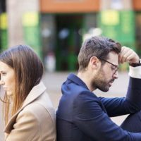 upset man and woman sitting outside back to back