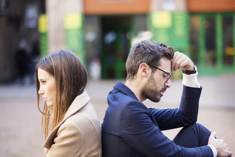 upset man and woman sitting outside back to back