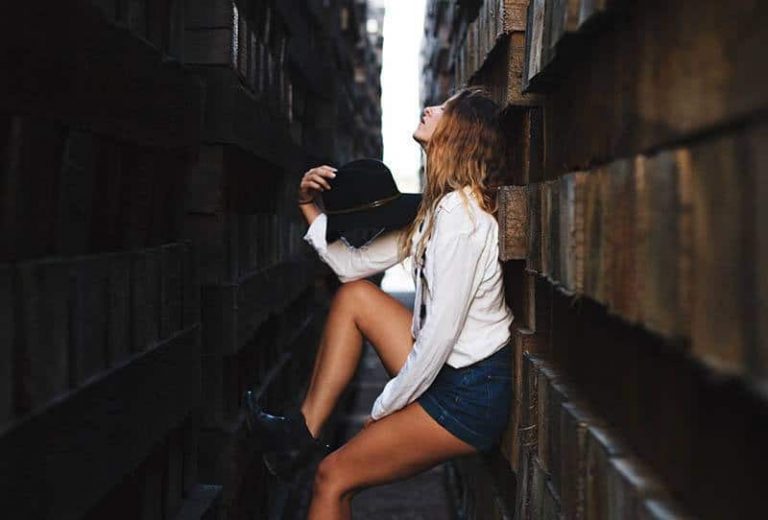 side view of woman holding hat between walls