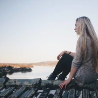 mujer sentada en un muelle gris cerca de una masa de agua