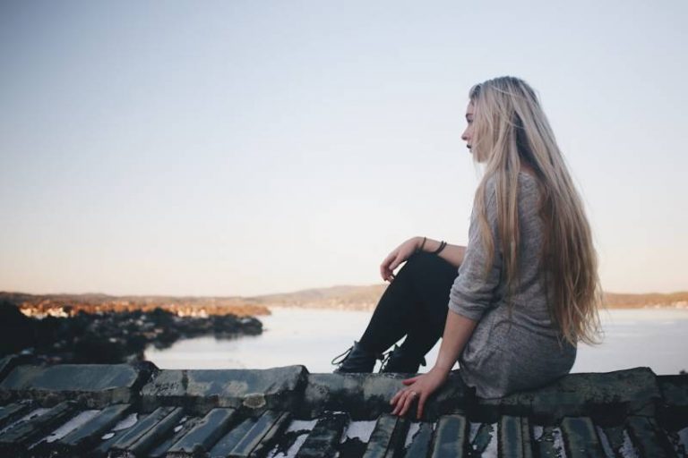 woman sitting on grey dock near body of water