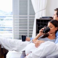 chill couple lying on couch in living room and drinking tea