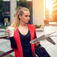 mujer elegante de pie al aire libre con la taza y los periódicos